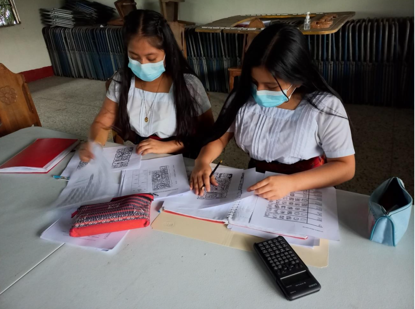 A couple of women wearing masks and looking at papers on a table

Description automatically generated with low confidence