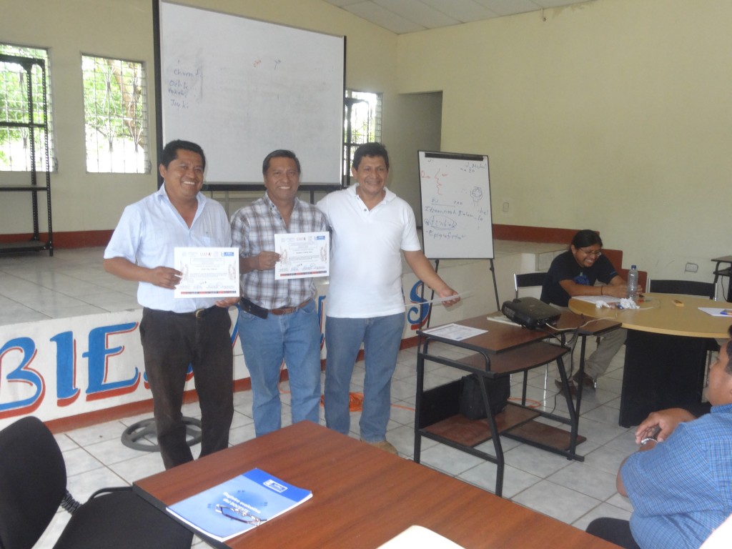 Romel Reyes, Director of Defensoría Q'eqchi', delivering certificates of participation to two teachers.